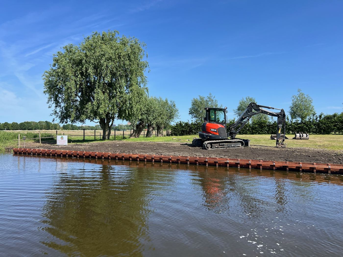 Graafmachine op een nieuwe beschoeiing langs een plas