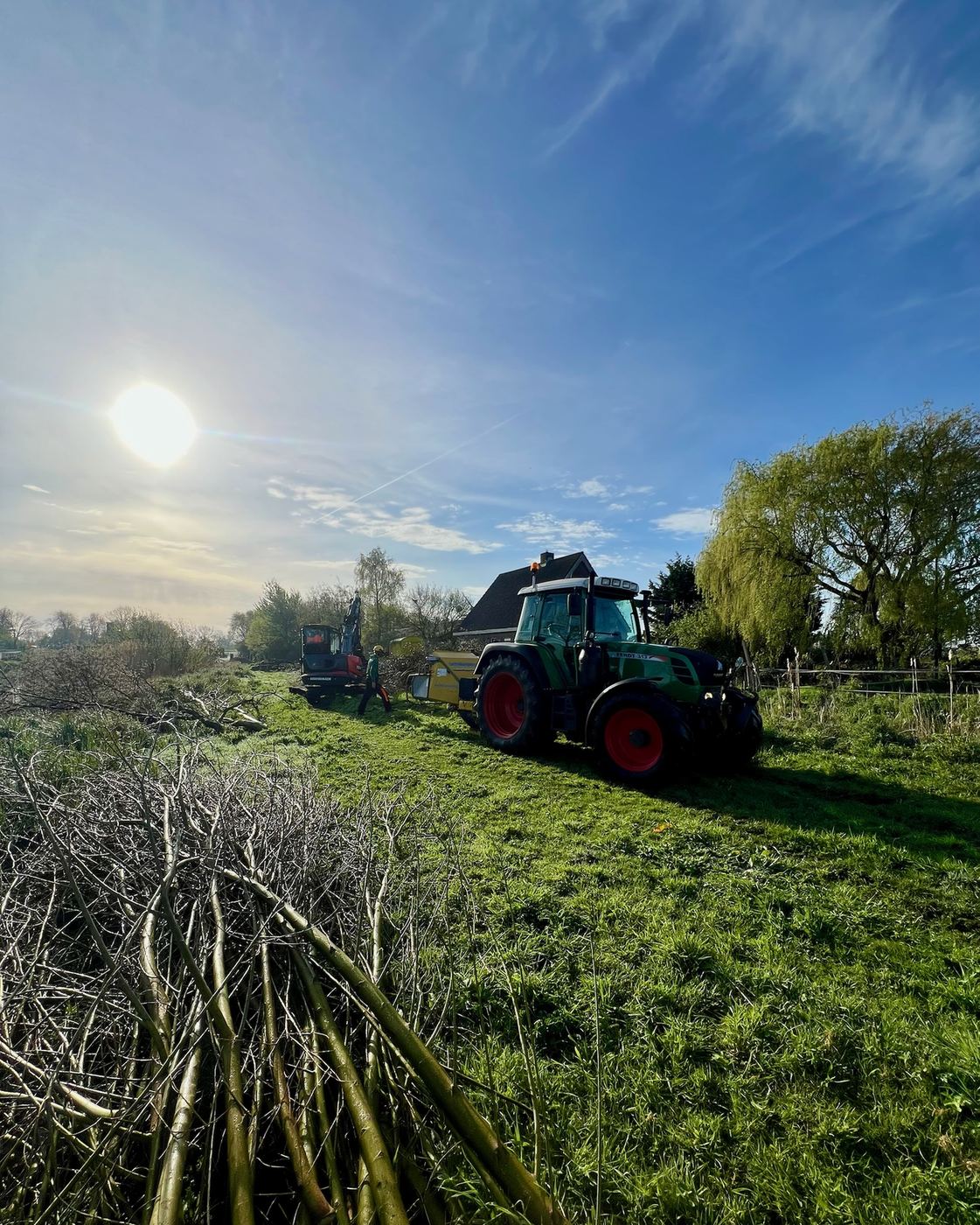 Tractor bij gesnoeide wilgentakken langs het water