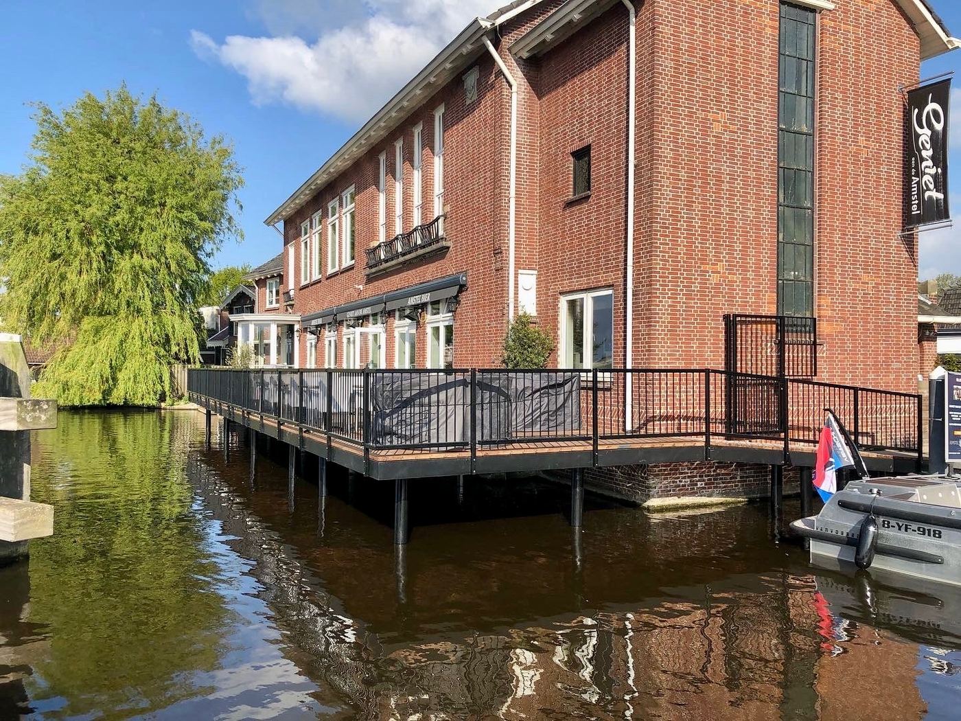 Houten terras met stalen hekwerk aan het water bij een bakstenen gebouw